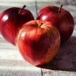 Close-up of fresh red apples on a rustic wooden table captured in natural light.